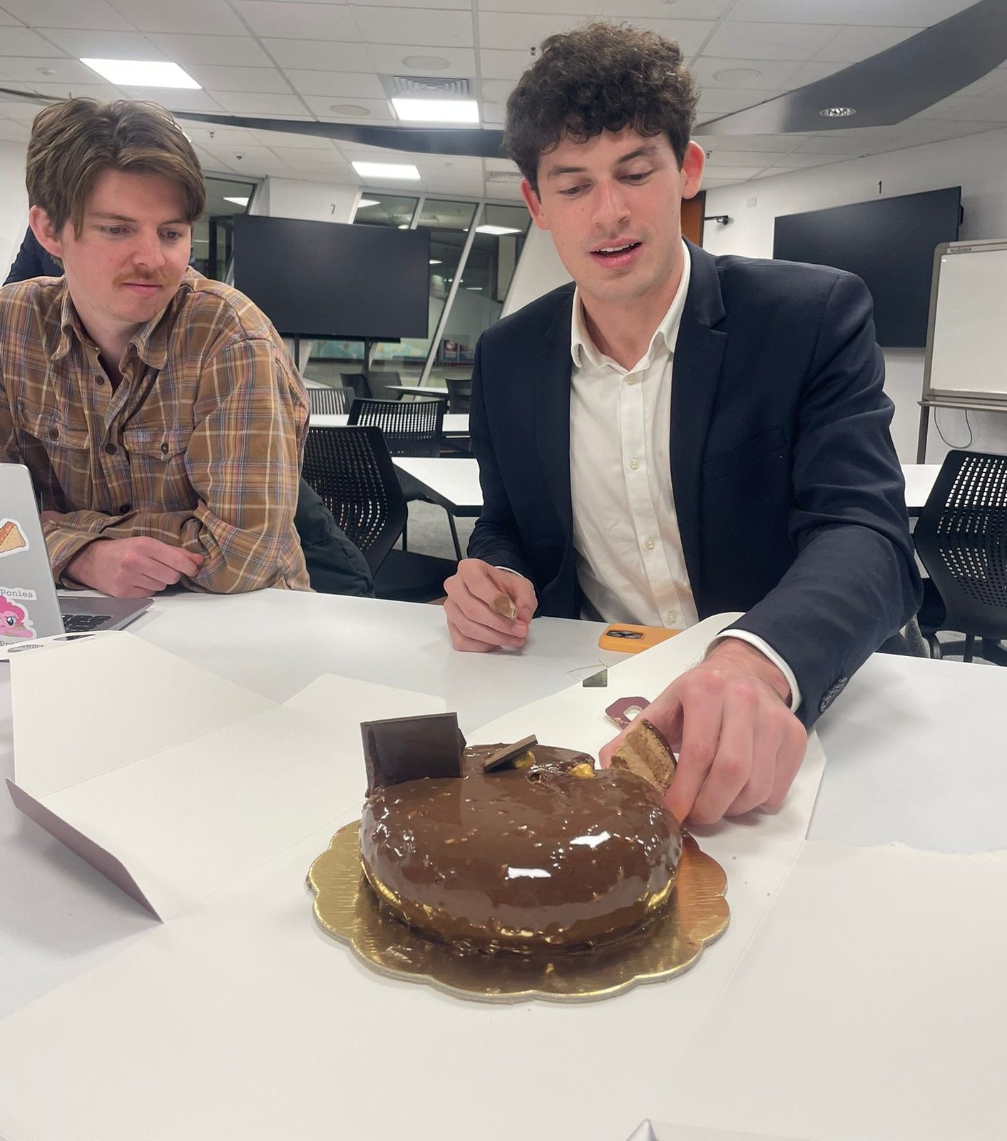 Noah with a colleague at a work celebration, cutting a cake in the office