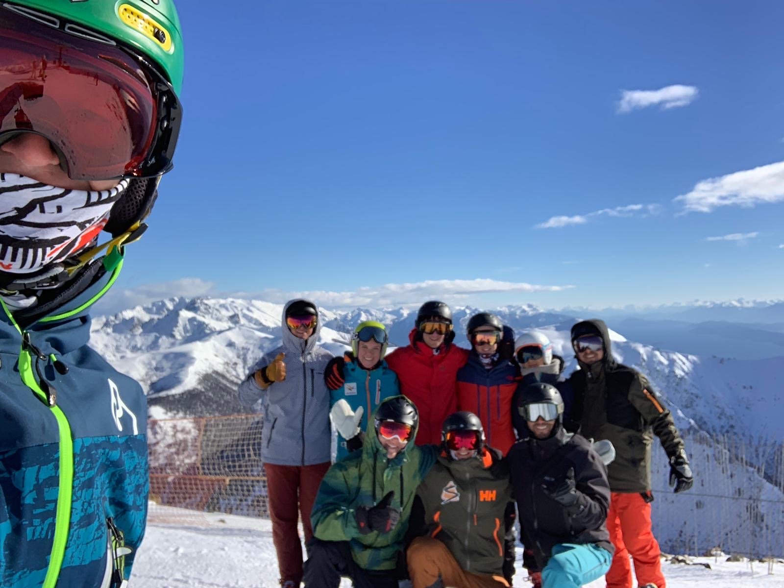 Noah and friends at the top of a ski run, snowy peaks behind